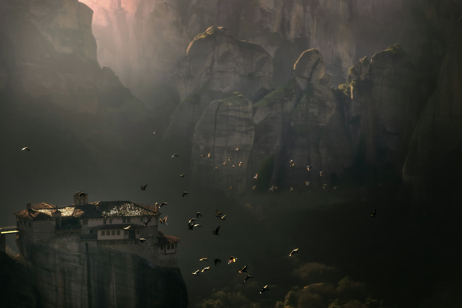 A Meteora monastery on its rock pillar in low cloud, birds circling below