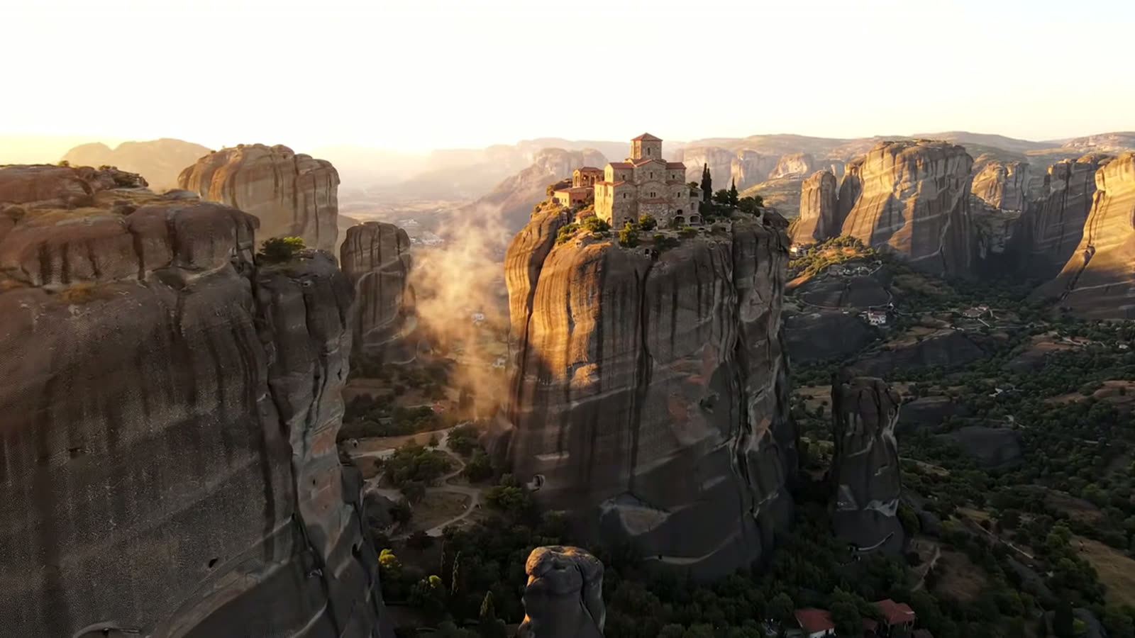 A monastery on a sandstone pillar at Meteora in the low golden light of late afternoon, mist drifting through the valley